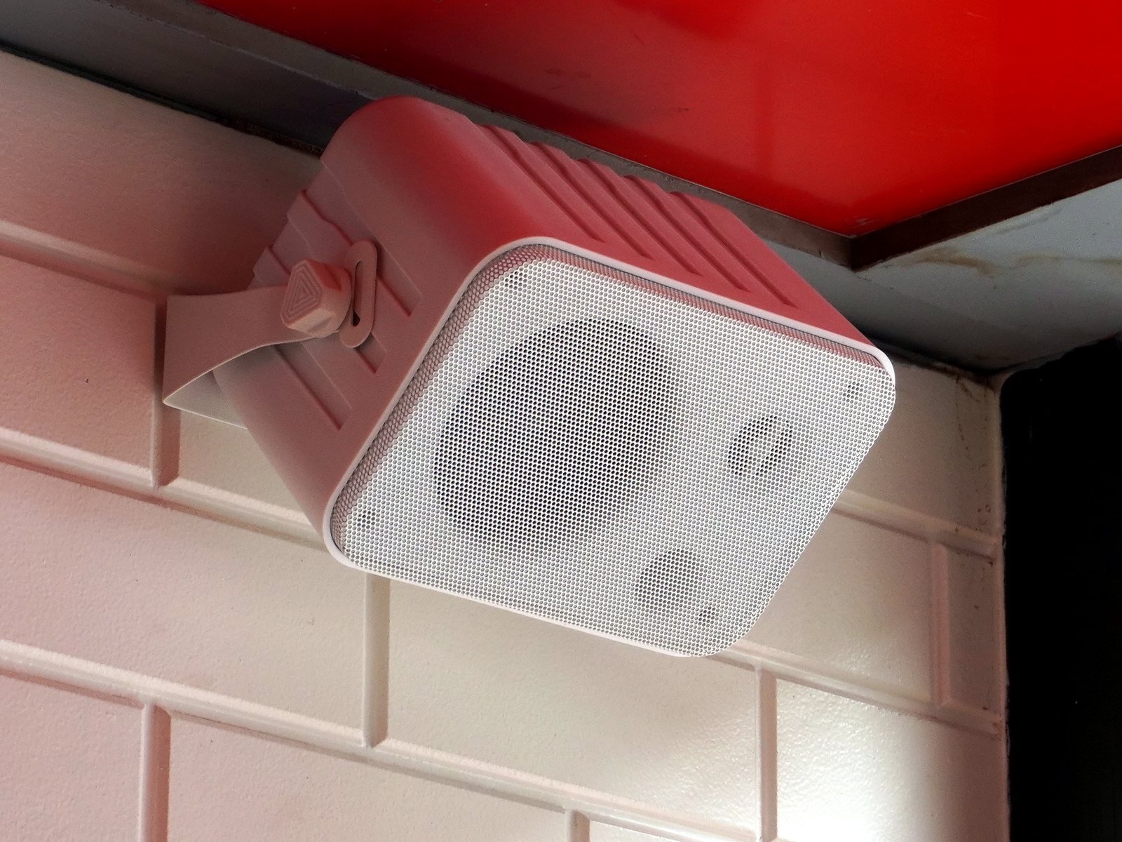 Wall-bracket speaker on white brick under a red ceiling in a Bandra burger restaurant
