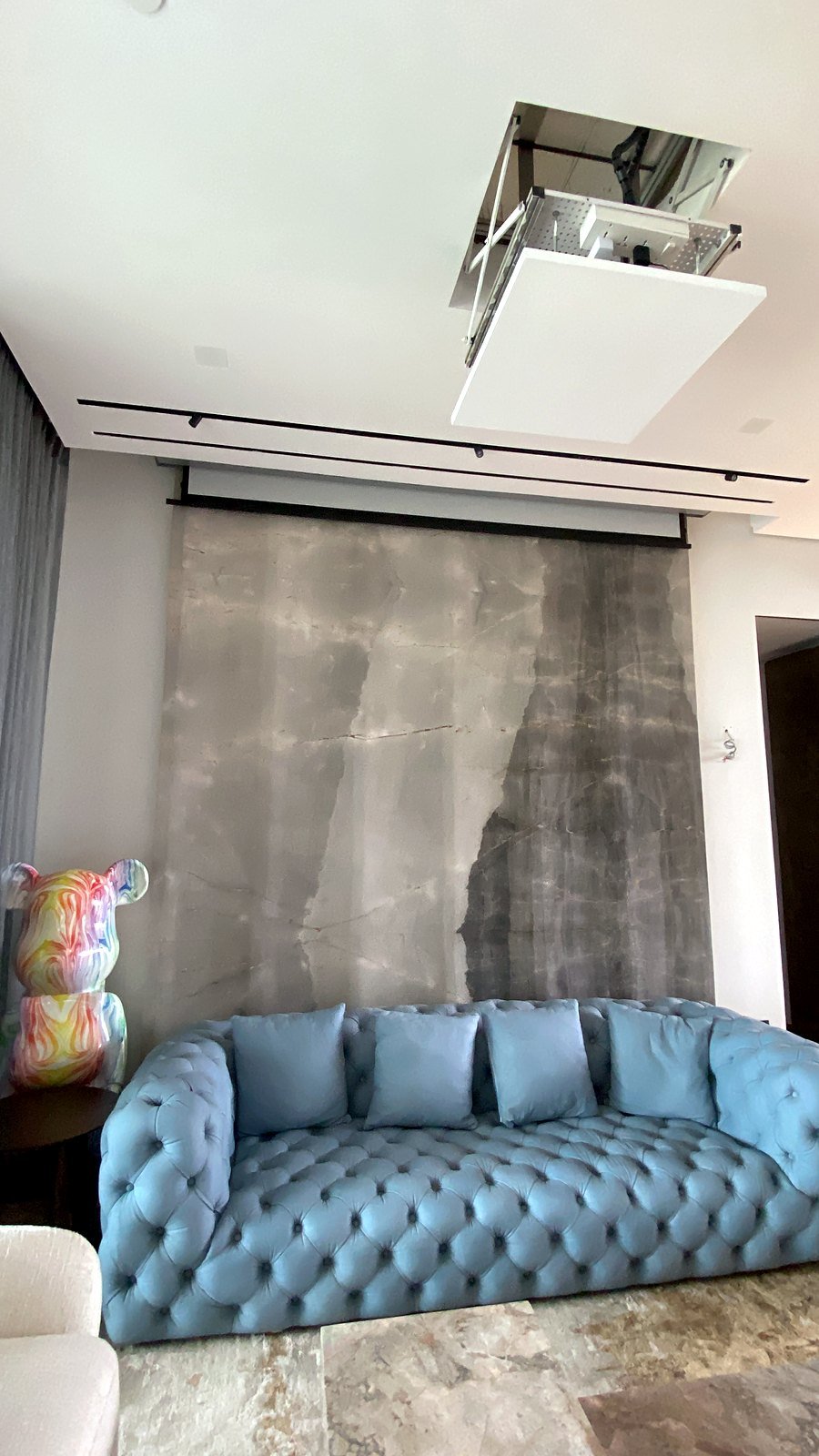 Projector lift lowered from the ceiling above the screen wall in a Bandra living room