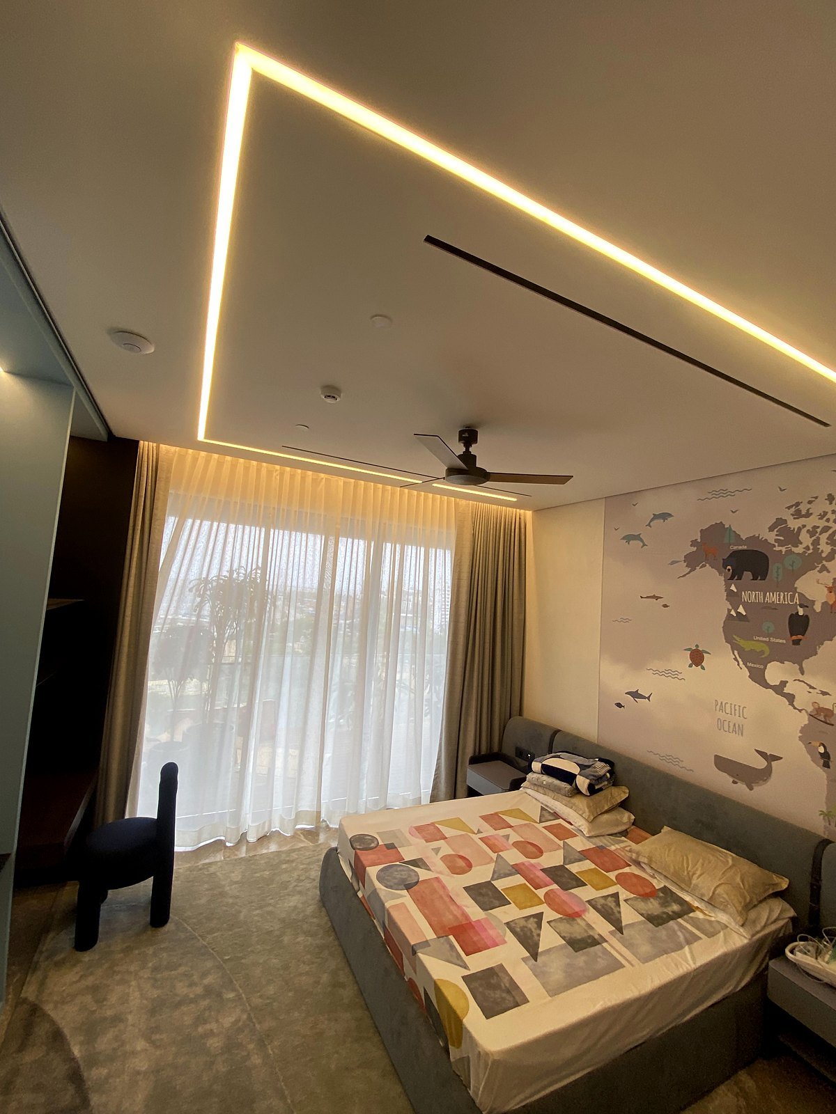 Bedroom in a Bandra apartment with cove lighting, curtains and a ceiling fan