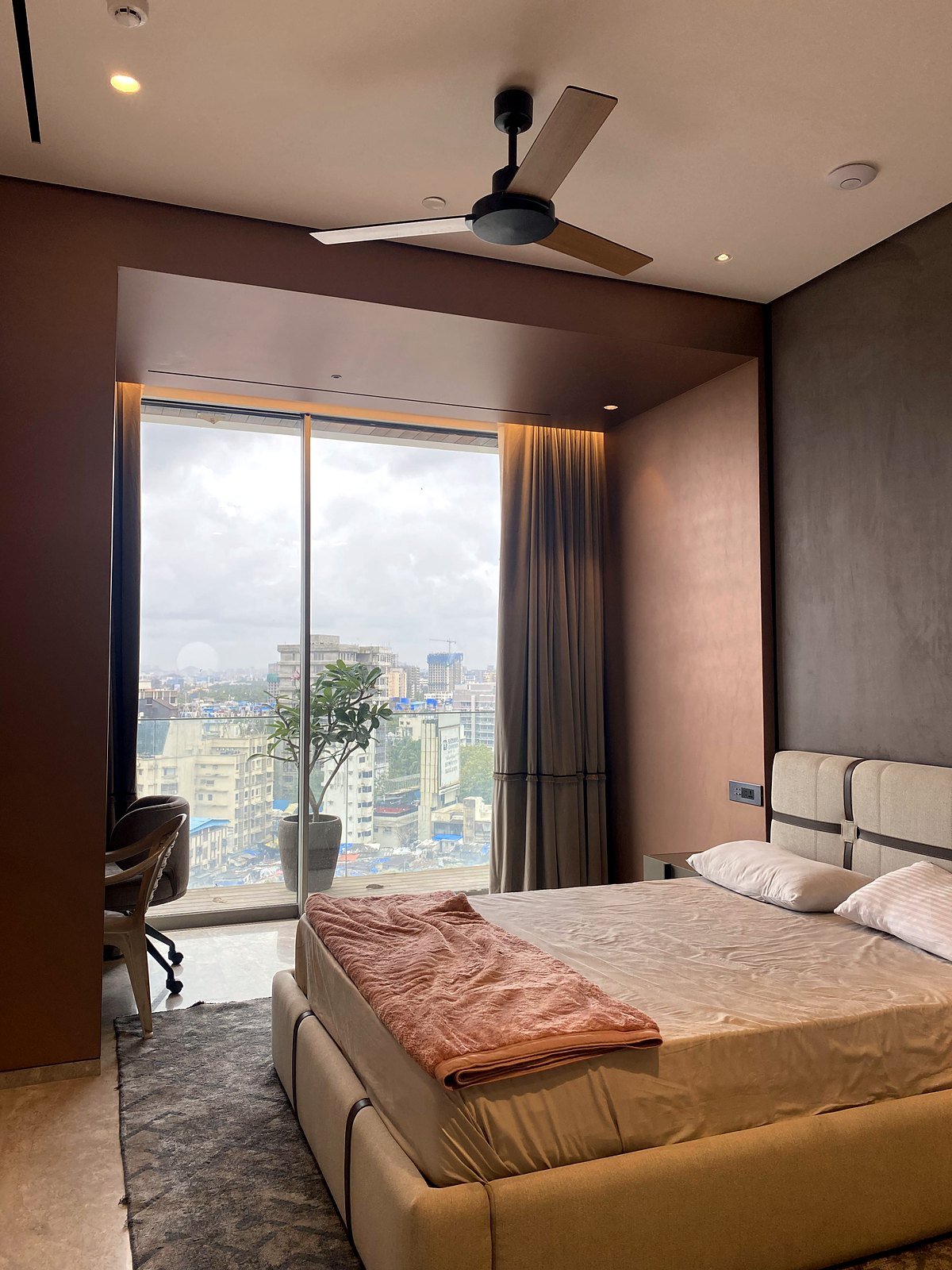 Bedroom in a Bandra apartment with a window, curtains and a ceiling fan