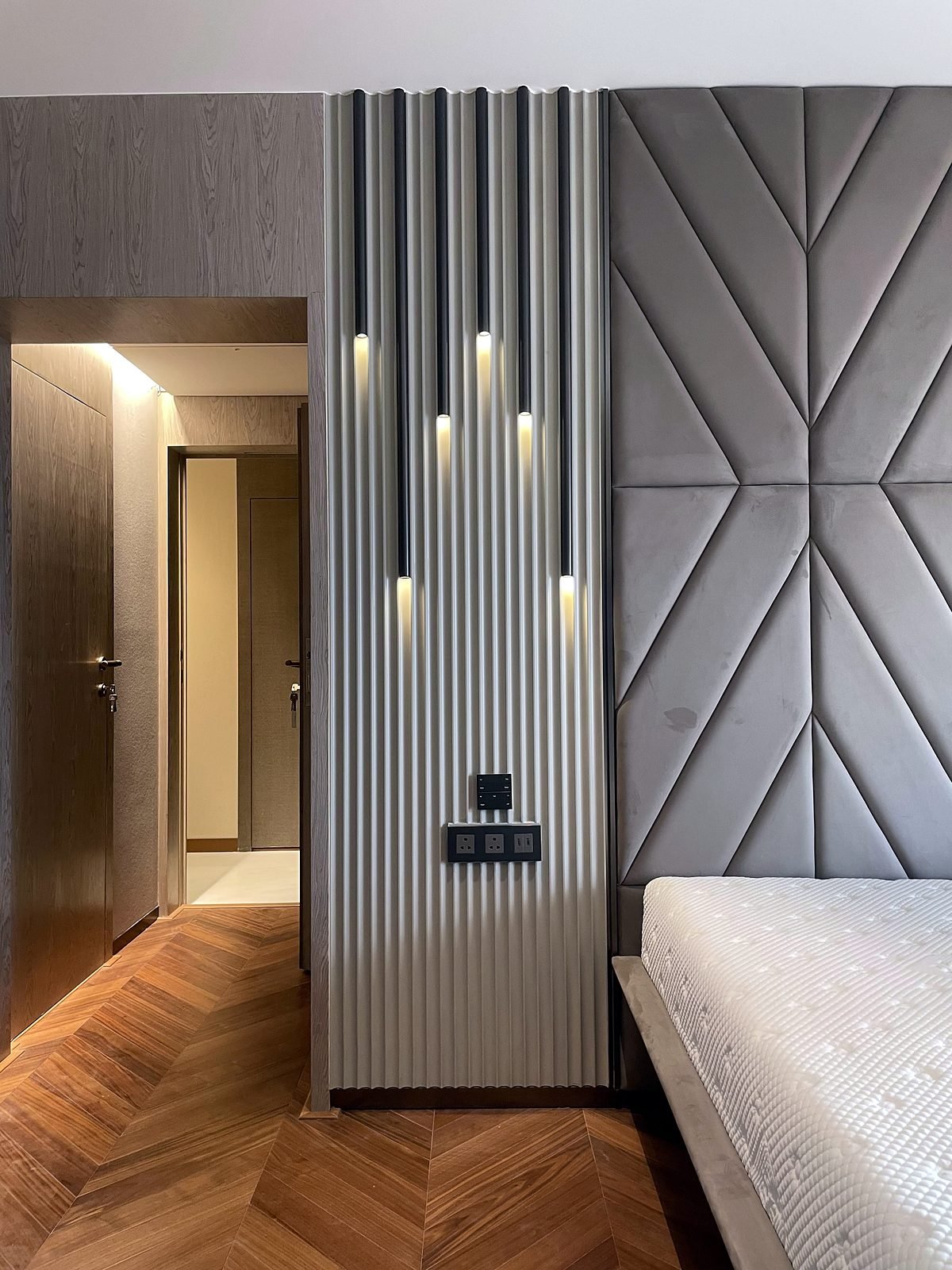 Bedroom in a Cuffe Parade apartment with a fluted wall, pendant lights and a herringbone wood floor