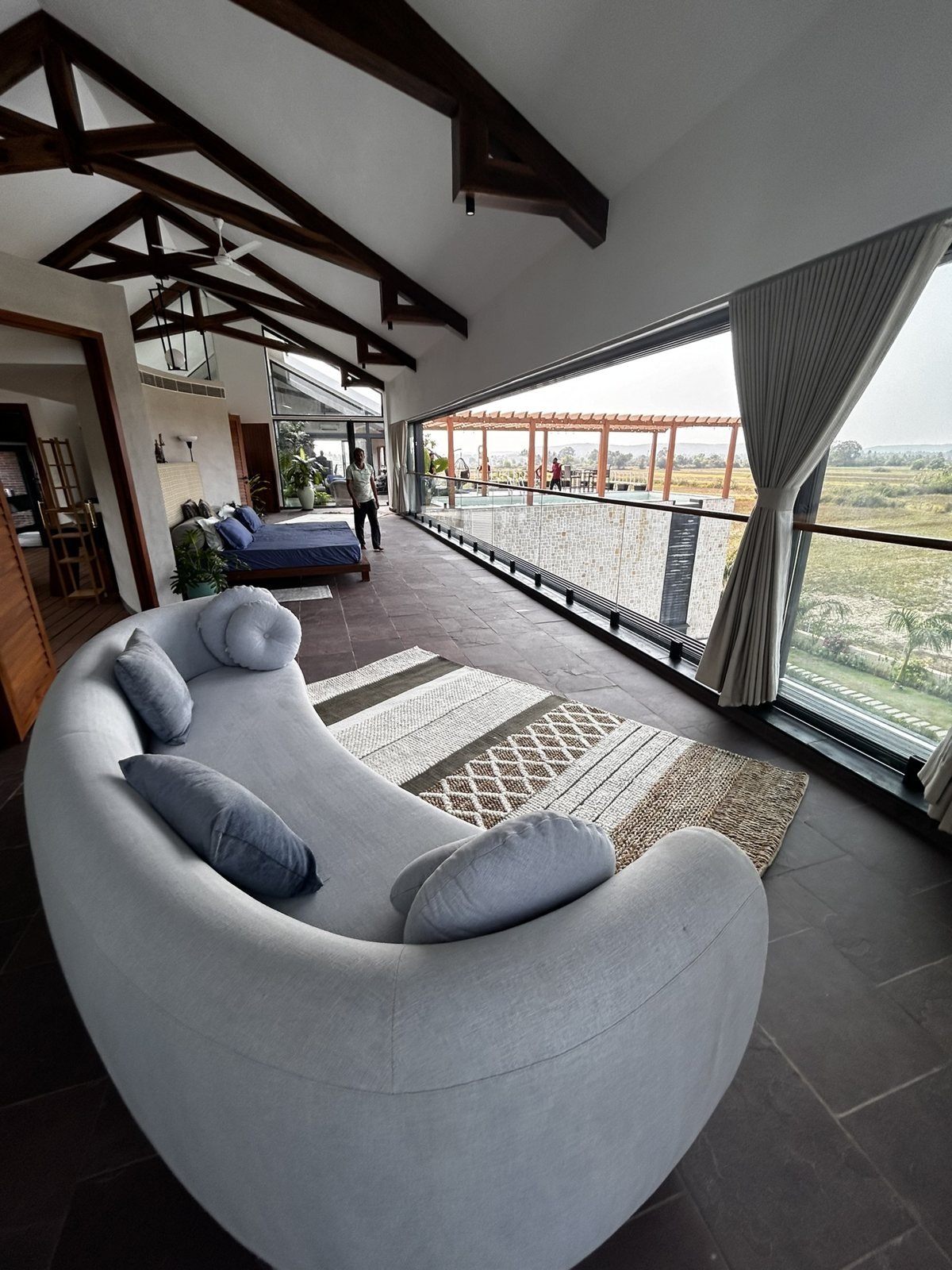 Curved sofa in a high-ceilinged villa lounge in Goa with exposed timber trusses