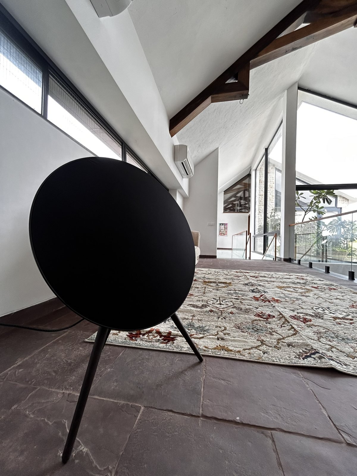Round black wireless speaker on a stand in a bright Goa villa living space