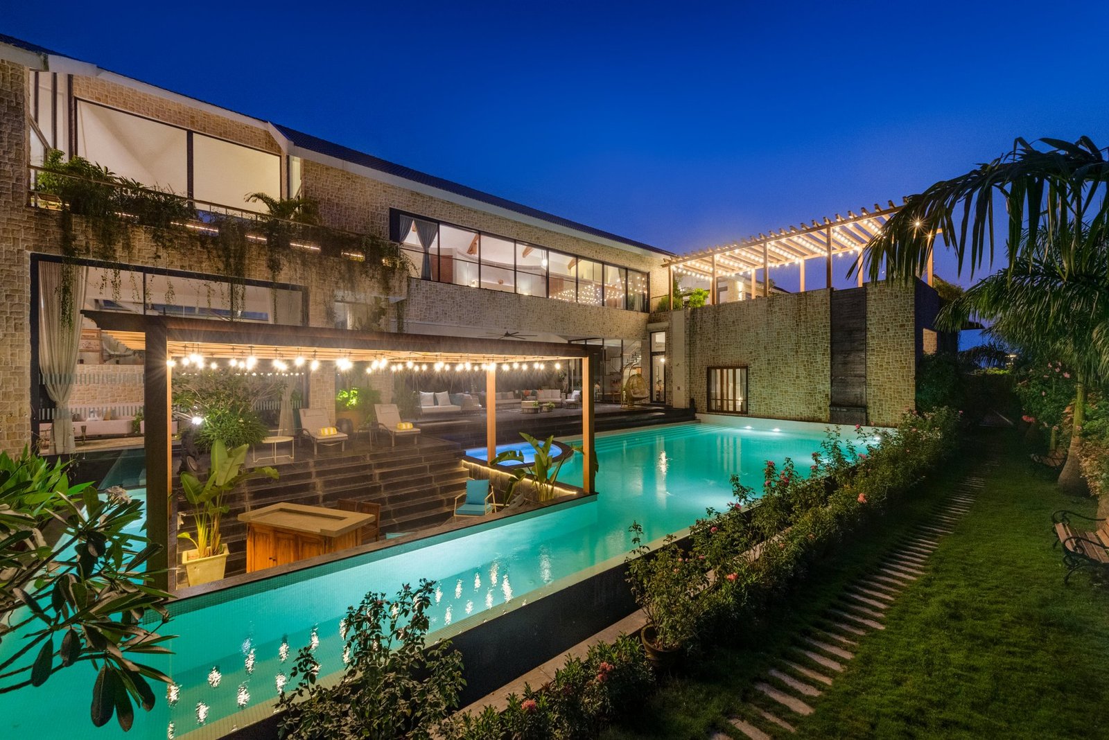 Villa pool terrace and glass-fronted rooms lit at night in Goa