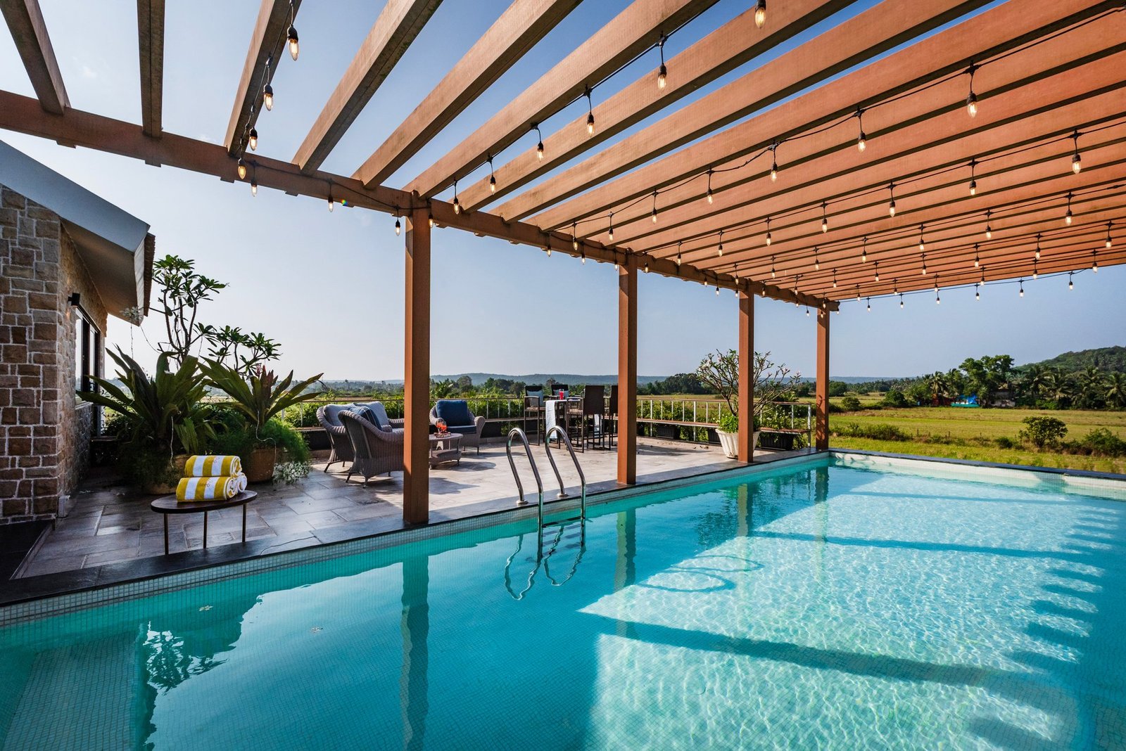 Swimming pool with a timber pergola and open fields beyond, Goa