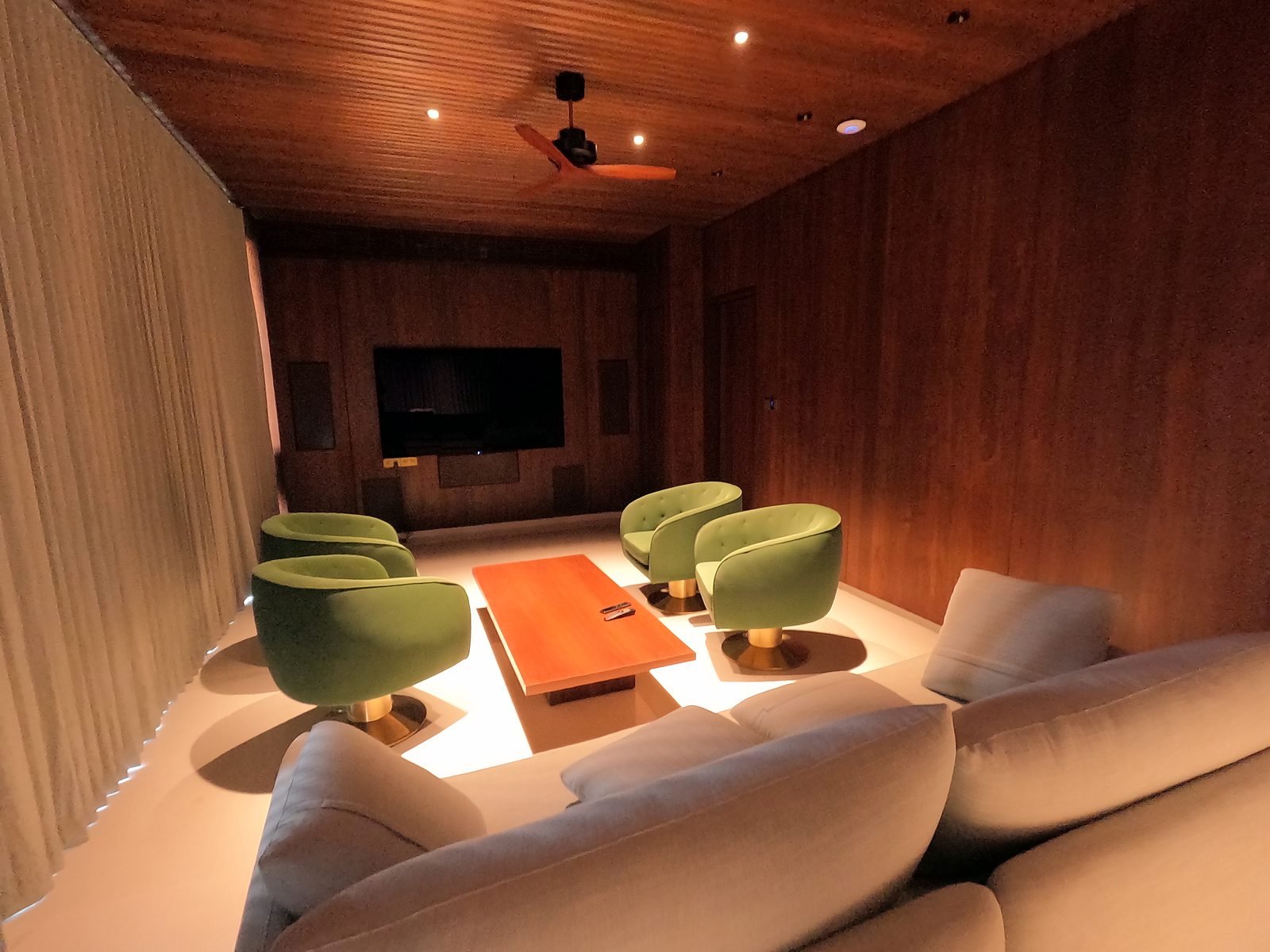 Wood-panelled lounge with wall-mounted TV and green armchairs in a Nagpur smart mansion